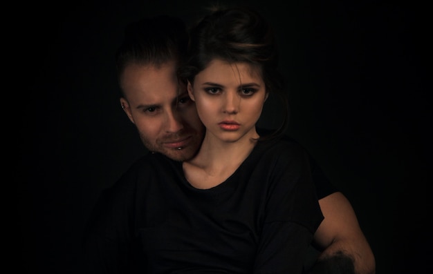 Sexy couple posing on dark cyclorama, guy with black hands hugs a beautiful girl