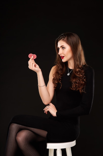 Sexy curly hair brunette posing with chips in her hands poker concept black background