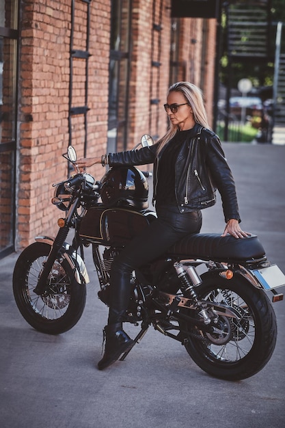 Sexy dramatic woman is parking her shiny new motorbike next to brick wall.