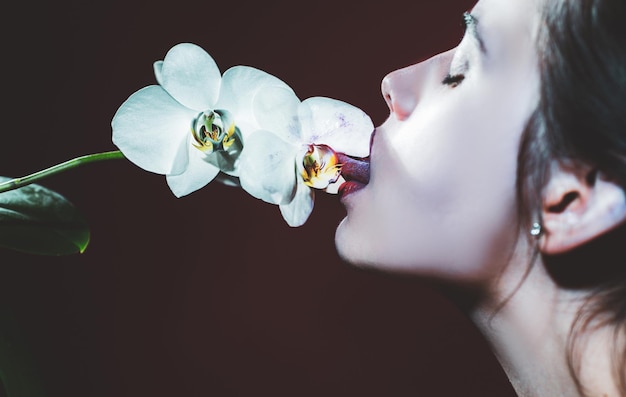 Sexy girl lick orchid flower Orchids oral tongue Sensual young woman suck floral orchidea Red lirs with lipstick