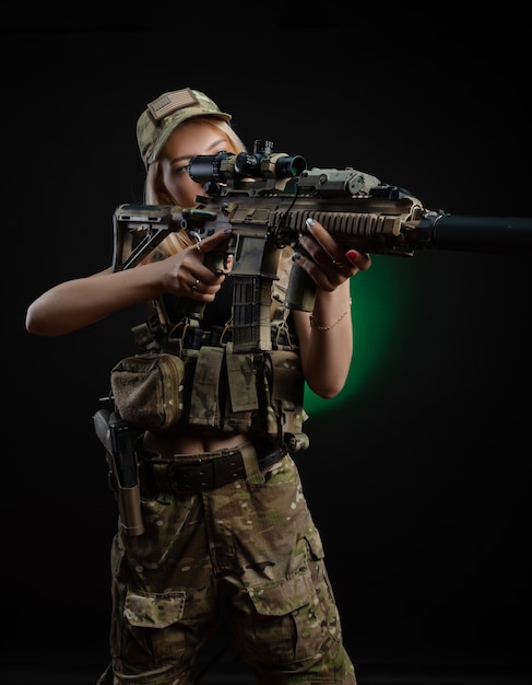 A sexy girl in military airsoft overalls poses with a gun in her hands on a dark background