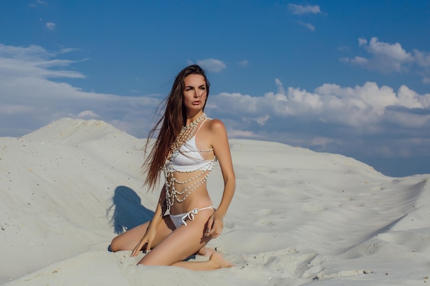 Sexy girl in the sand in a white bikini