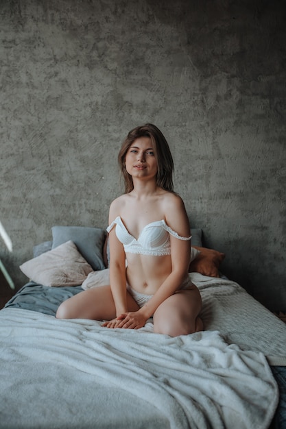 Sexy girl sitting on bed in white lingerie