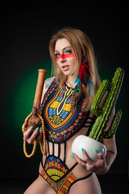 Sexy hippie girl posing with bong for smoking marijuana in a bright swimsuit on a dark background