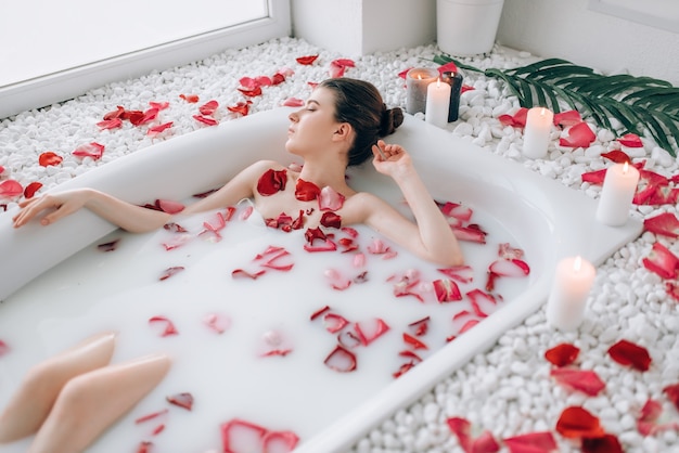 Sexy lady lying in bath with foam and rose petals