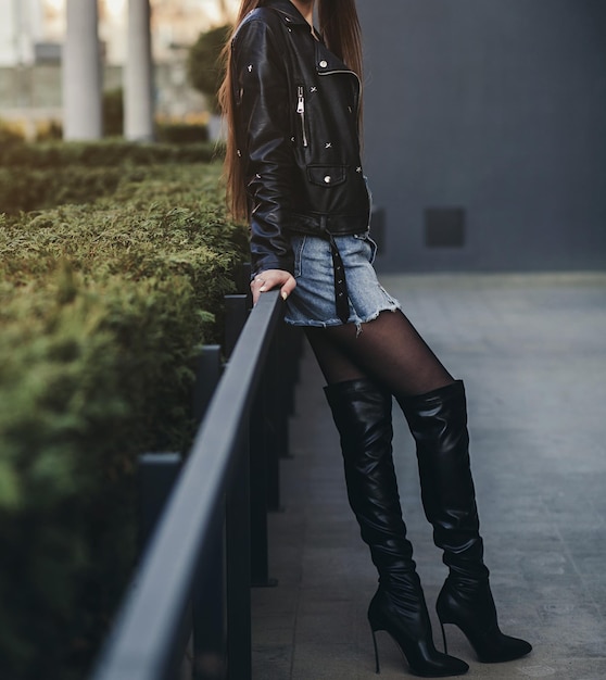 Sexy model in a leather jacket and long legs poses in boots