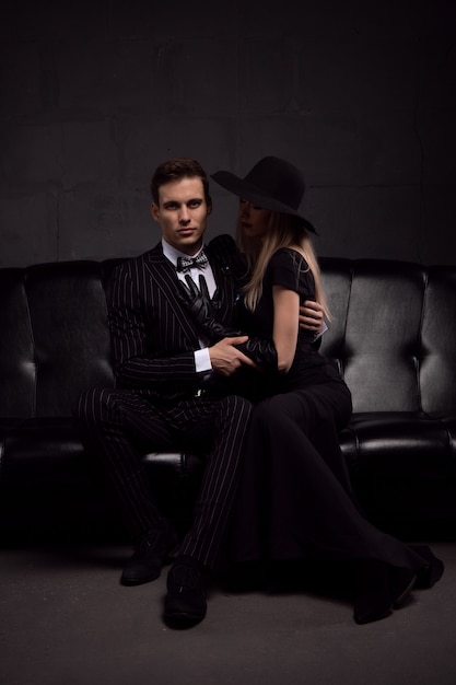 Sexy passionate couple in elegant evening dresses on a dark sofa in a room with low light