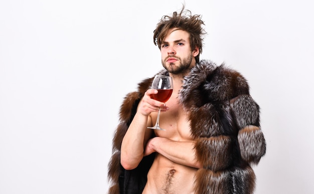 Sexy sleepy rich macho tousled hair drink wine isolated on white Fashion and pathos Richness and luxury concept Guy attractive rich posing fur coat on naked body Rich athlete enjoy his life