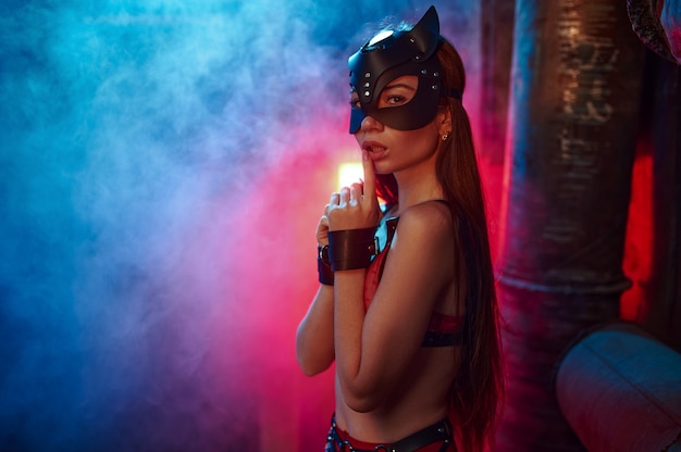 Sexy woman poses in bdsm suit and leather cat mask, abandoned factory interior. Young girl in erotic underwear, sex fetish, sexual fantasy