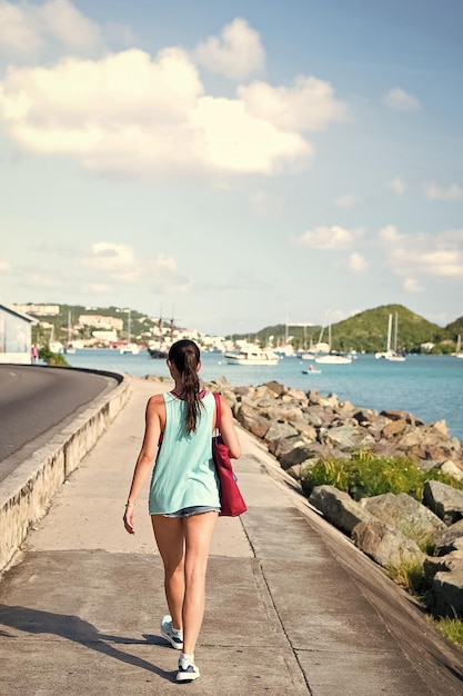 Sexy woman walk along sea in stthomas british virgin island Woman in top and shorts on sea side promenade on sunny day back view beach fashion Summer vacation on island wanderlust