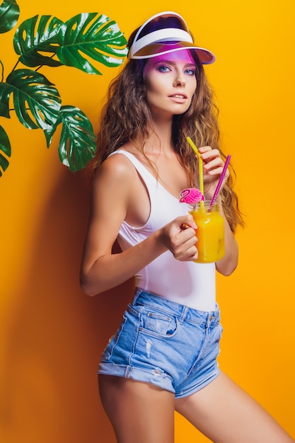 Sexy Woman in white swimsuit and blue jeans shorts, trendy visor holding beverage