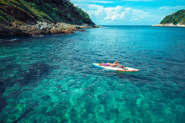 Sexy, woman with a beautiful body posing while lying in a bikini on a surfboard