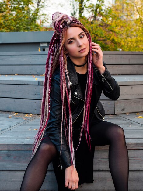 Sexy woman with pink long dreadlocks hairstyle in black clothes looking at the camera shot in autumn