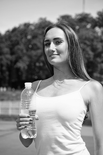 Sexy woman with plastic bottle on stadium Woman with water bottle on sunny outdoor Drinking water for health Thirst and dehydration Sport activity and energy