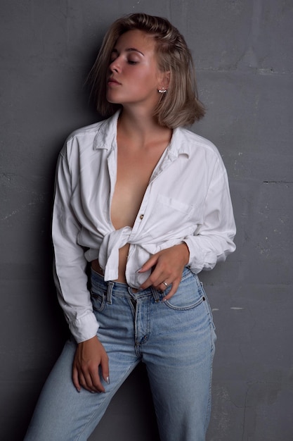 Sexy young blonde with a beautiful figure in jeans and an unbuttoned shirt