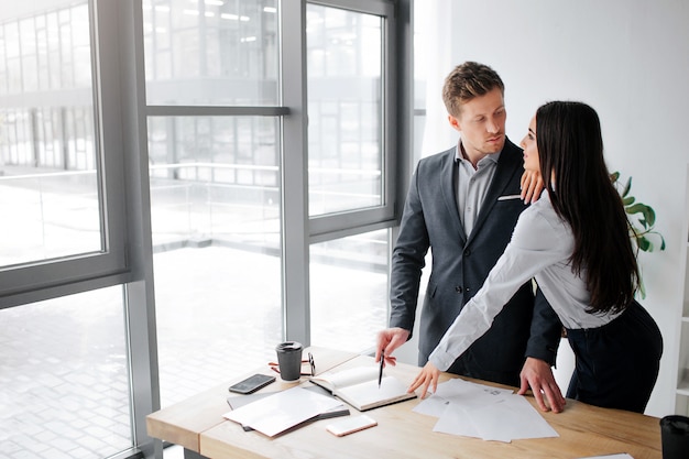 Sexy young woman stand close to her boss and look at him. She touch his shoulder.