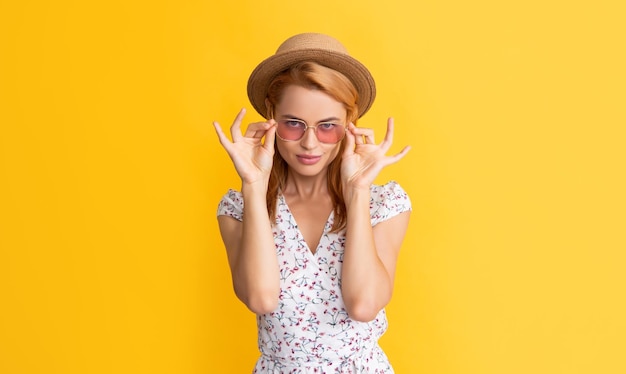 Sexy young woman in straw hat and sunglasses on yellow background