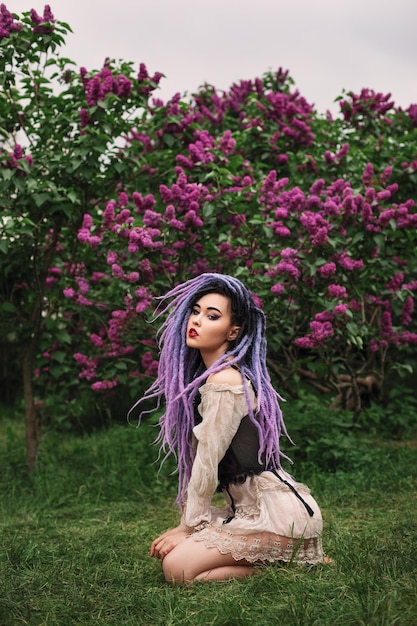 sexy young woman with color dreadlocks, in corset is sitting under the lilac