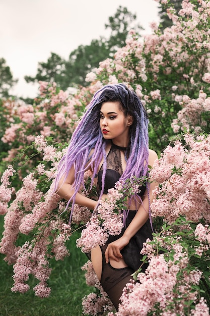 sexy young woman with color dreadlocks is sitting among the blooming tree