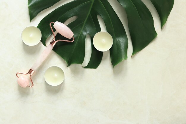 sFacial beauty massage spa selfcare concept Massage roller on a monstera leaf candles top view