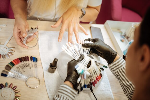 Shade of beige. Blonde-haired constant beautiful client of professional nail artist choosing shade of beige color