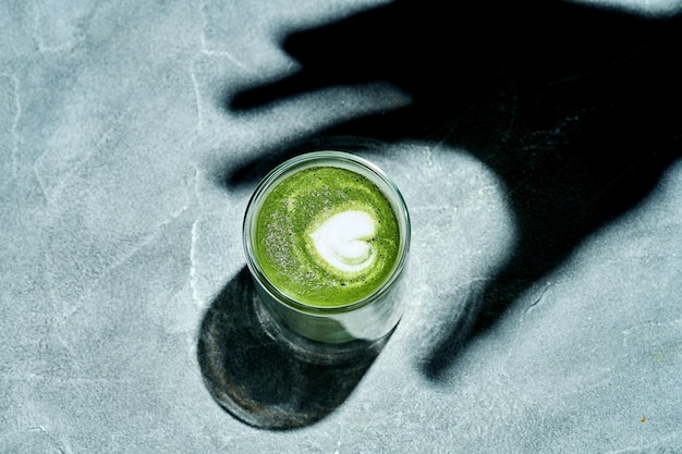 Shadow of a hand reaching out to grab a matcha latte on a concrete background