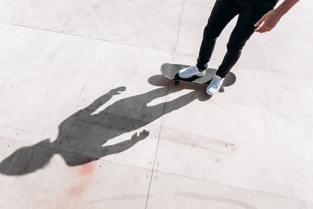 The shadow of the man standing on the skateboard on the floor of slide in a skate park at the sunny day outside .