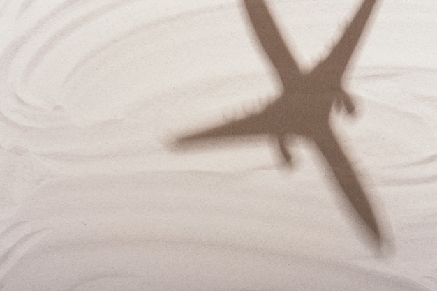 Shadow of plane or airplane on white sand background. Flat lay design. Travel, vacation concept