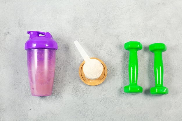 Shaker dumbbells and Measuring scoop of protein powder on gray concrete background