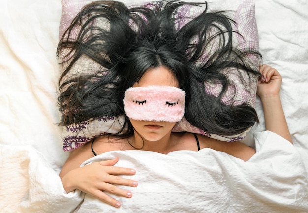 Shallow focus closeup of a female wearing a sleeping eye cover while lying on the bed