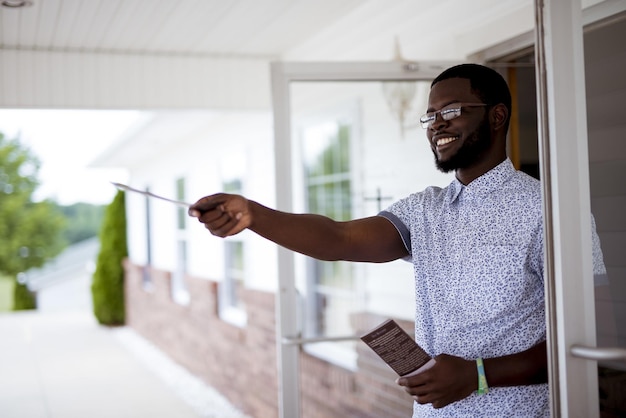 Shallow focus shot of a male standing near a door and giving out pamphlets  while smiling