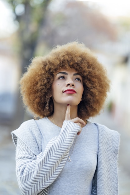 Shallow focus of a thoughtful curly-haired Hispanic female touching her chin in a park