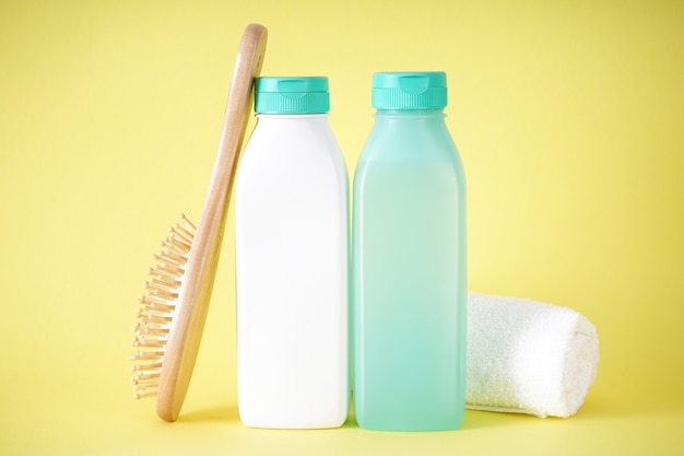 Shampoo, bottle of hair conditioner and wooden hair brush on yellow background.