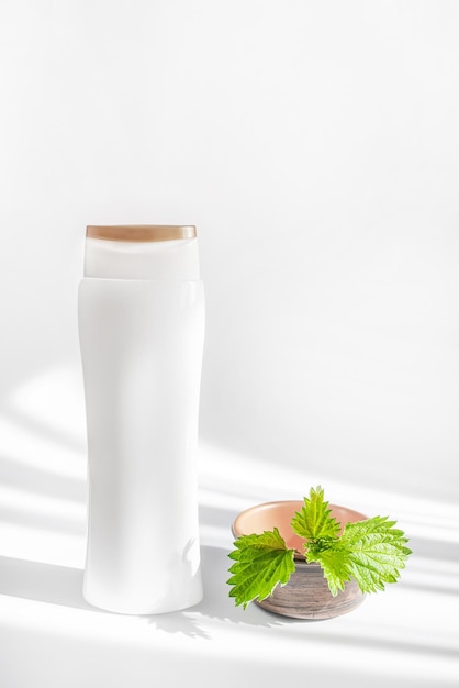 Shampoo bottle mockup on whihe background with trend shadows Natural cosmetics from nettles