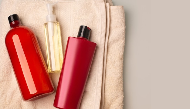 Shampoo, conditioner and cleansing oil lying on a bath towel in a bathroom. Space for text