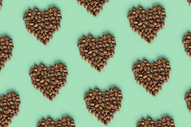 Shape heart from coffee bean on mint color background roasted brown coffee berries geometric pattern