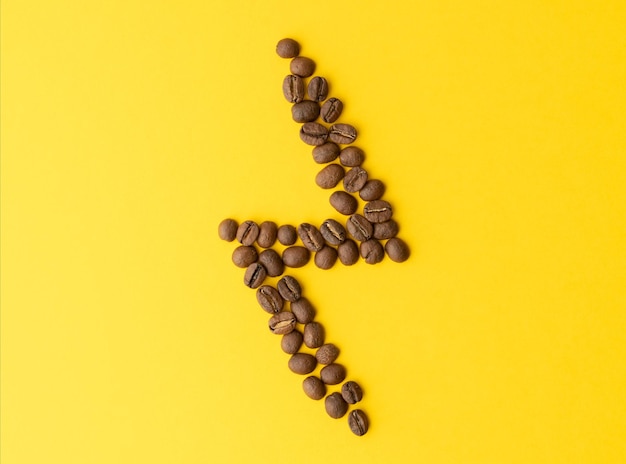 Shape of lightning made from roasted coffee beans on yellow background Coffee symbol concept