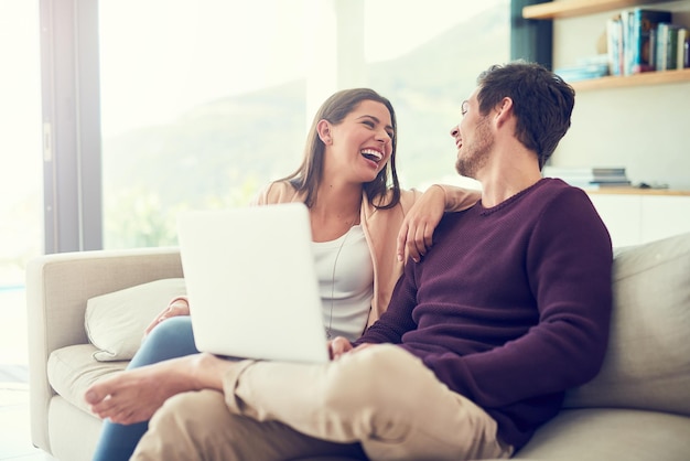 Sharing an online laugh Shot of a smiling young couple using a laptop while relaxing on the sofa at home