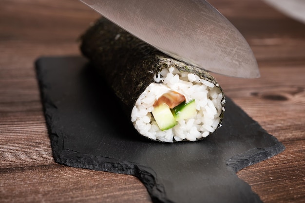 A sharp knife cuts a rolledup sushi roller