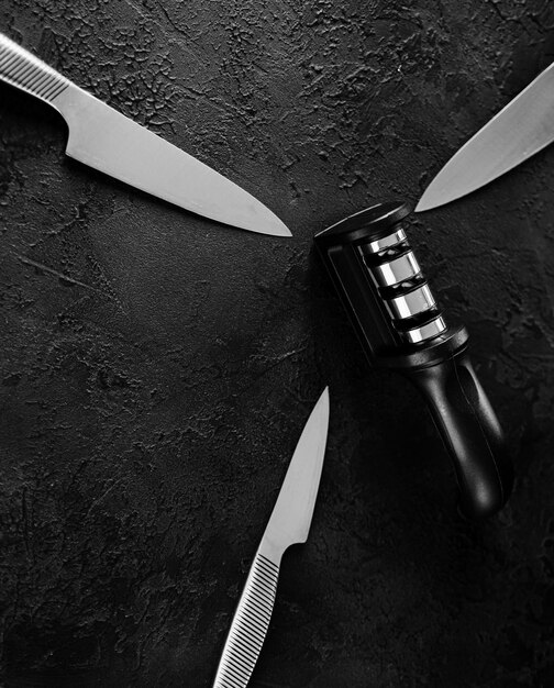 Photo sharp stainless steel metal knifes and a hand sharpener on a dark table