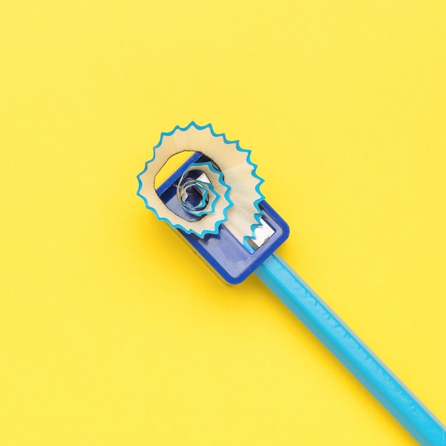 Sharpening a blue pencil with a hand sharpener on a yellow background. The minimum concept of education. Flat lay.