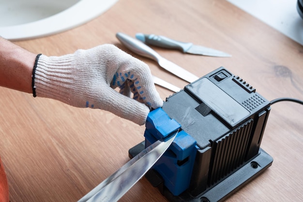 Sharpening a knife on an electric sharpener at home The man's hand drives the knife blade between the blue sharpeners dust flies on the machine