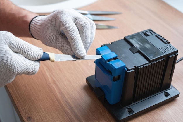 Sharpening a knife on an electric sharpener at home The man's hand drives the knife blade between the blue sharpeners dust flies on the machine