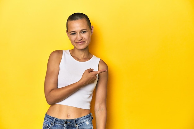 Shaved head woman smiling and pointing aside showing something at blank space