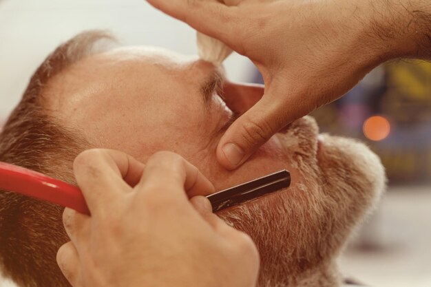 Shaving with straight razor in barbershop bearded man being shaved in barbershop