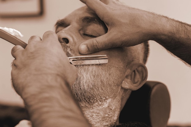 Shaving with a straight razor in a barbershop A bearded old man being shaved in a barbershop