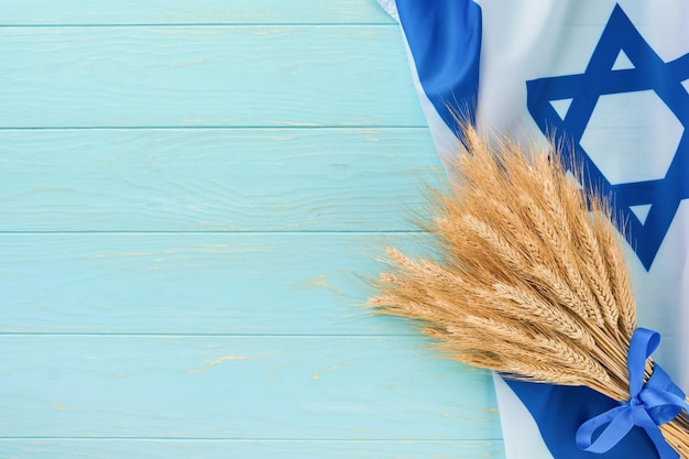 Photo shavuot jewish background ripe bouquet of wheat with blue ribbon with israel flag and backgrounds symbols of jewish holiday shavuot concept background for shavuot celebration top view mock up