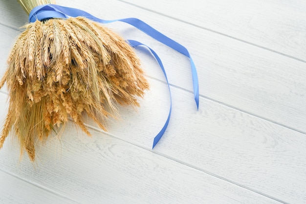 Shavuot jewish holiday celebration Bouquet of golden ripe wheat with a blue ribbon White wood board table with field of wheat Background for Shavuot celebration Top view Mock up