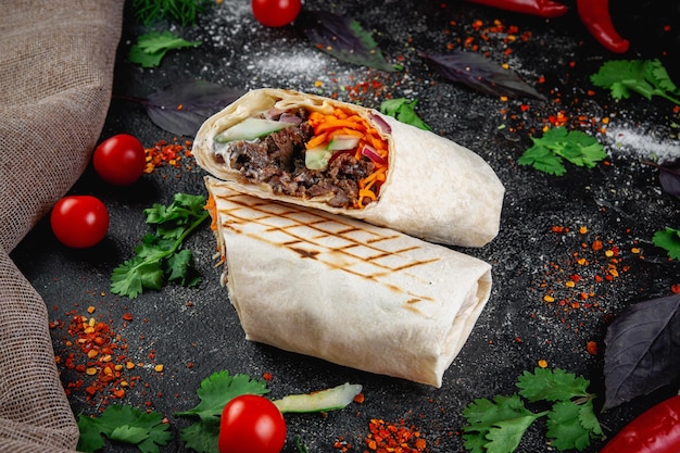 Shawarma burrito cut with vegetables and herbs on a dark stone table The concept of fast food restaurants