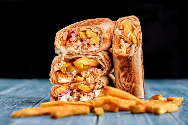 Shawarma chicken roll in a pita with fresh vegetables cream sauce and french fries on wooden backgro...